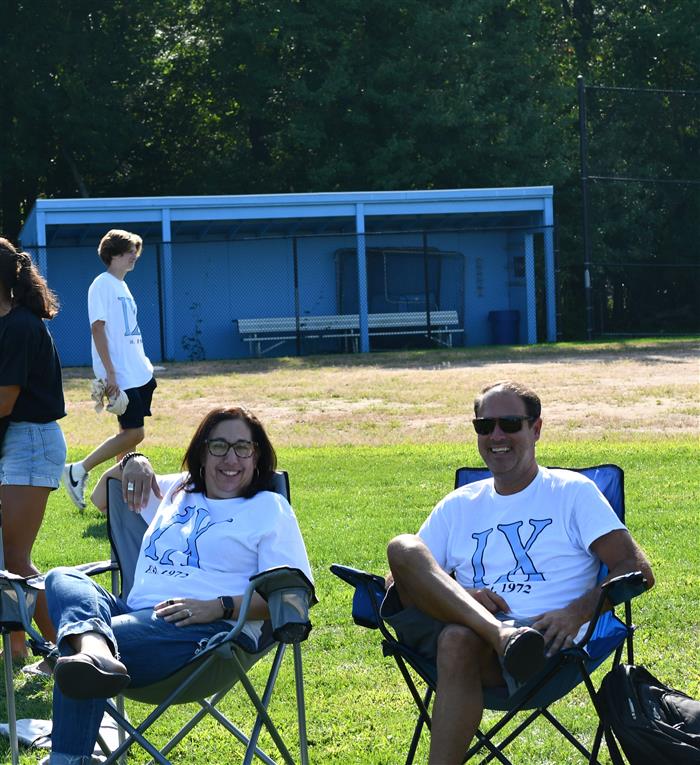 Man and woman sit on the side of field, wearing Title IX shirts
